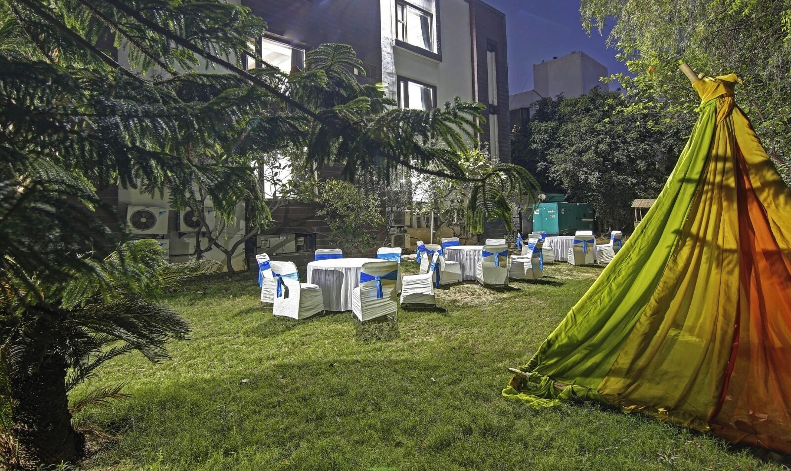 An outdoor seating area with white tables and chairs, a green tent, and a grassy lawn.