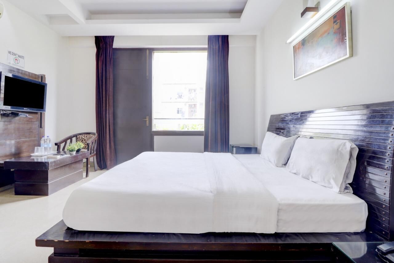 A hotel room with a bed, a TV, a desk, a chair, and a window with curtains.