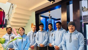A group of people in light blue hoodies standing indoors with a staircase and a plant in the foreground. - Blue Moon Residency Hotel & Restaurant (Gurugram)