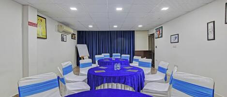 A conference room with round tables, white chairs with blue sashes, and blue tablecloths.