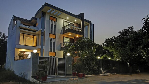 A modern two-story house with a balcony, large windows, and a gated entrance. - Blue Moon Residency Hotel & Restaurant (Gurugram)