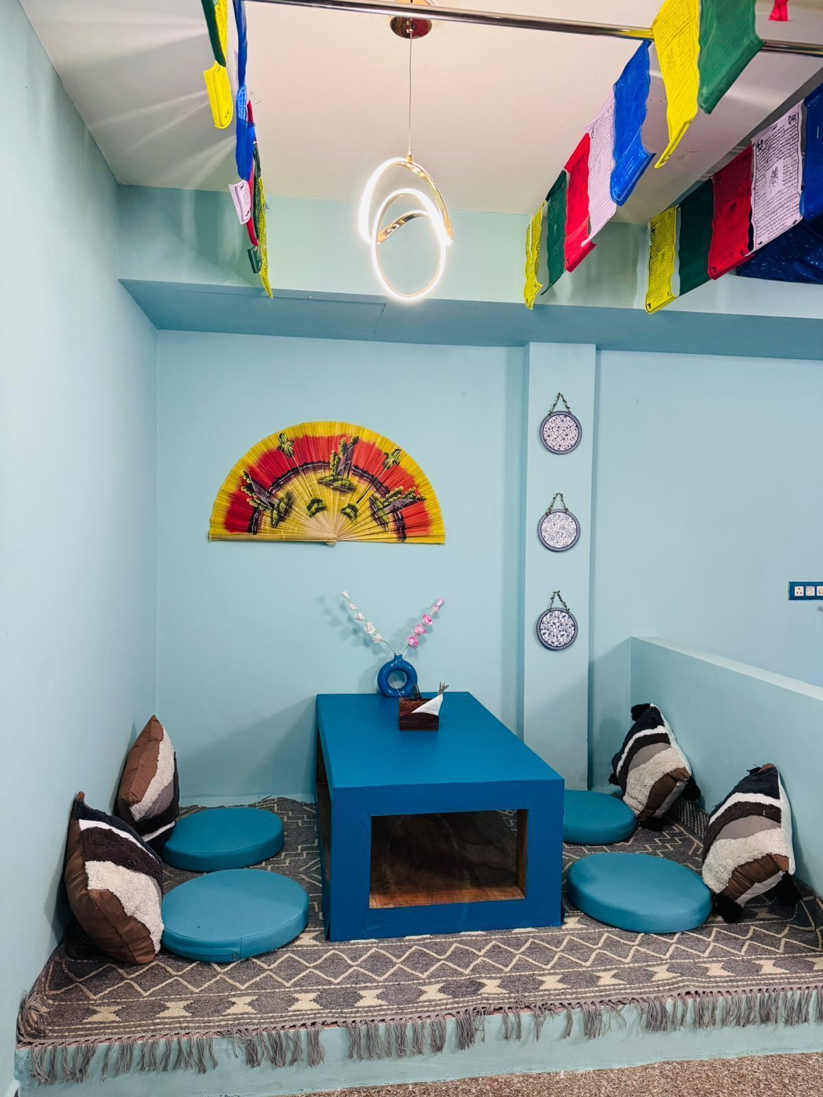 Una habitación con un sofá azul, una mesita con un florero y un tapiz de colores.