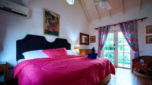 A bedroom with a large bed, a ceiling fan, a window with curtains, and a painting on the wall. - Charming 3-bedroom Gingerbread Style Villa in Bon Accord, Tobago (Bon Accord)