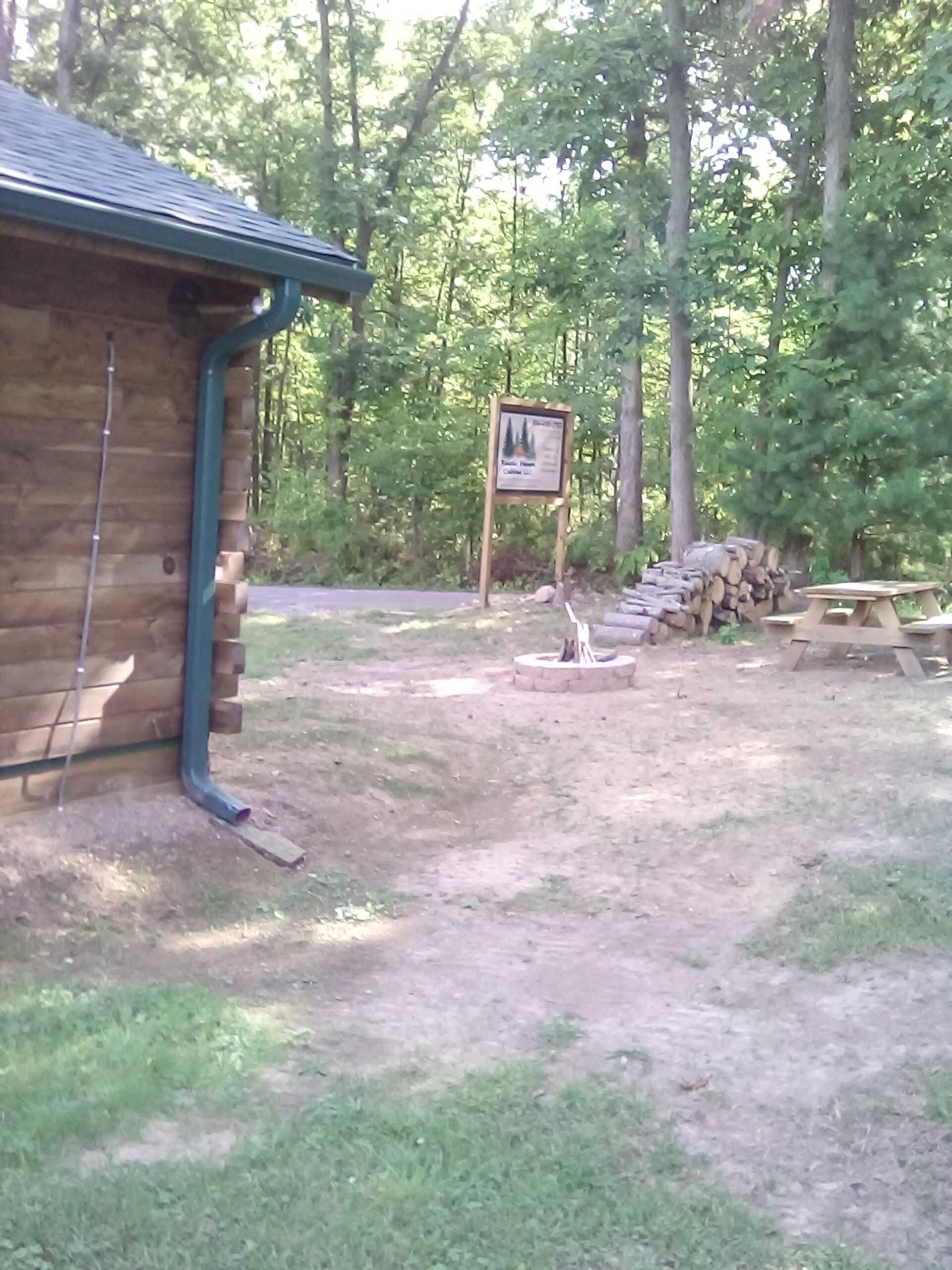 Een rustieke hut met een houten gevel en een metalen dak. Op de achtergrond staat een naambordje en in de buurt een picknicktafel.
