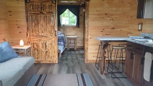 Ein gemütliches Blockhaus-Interieur mit Bett, einem kleinen Tisch, einer Bar und einem Fenster mit Vorhängen.