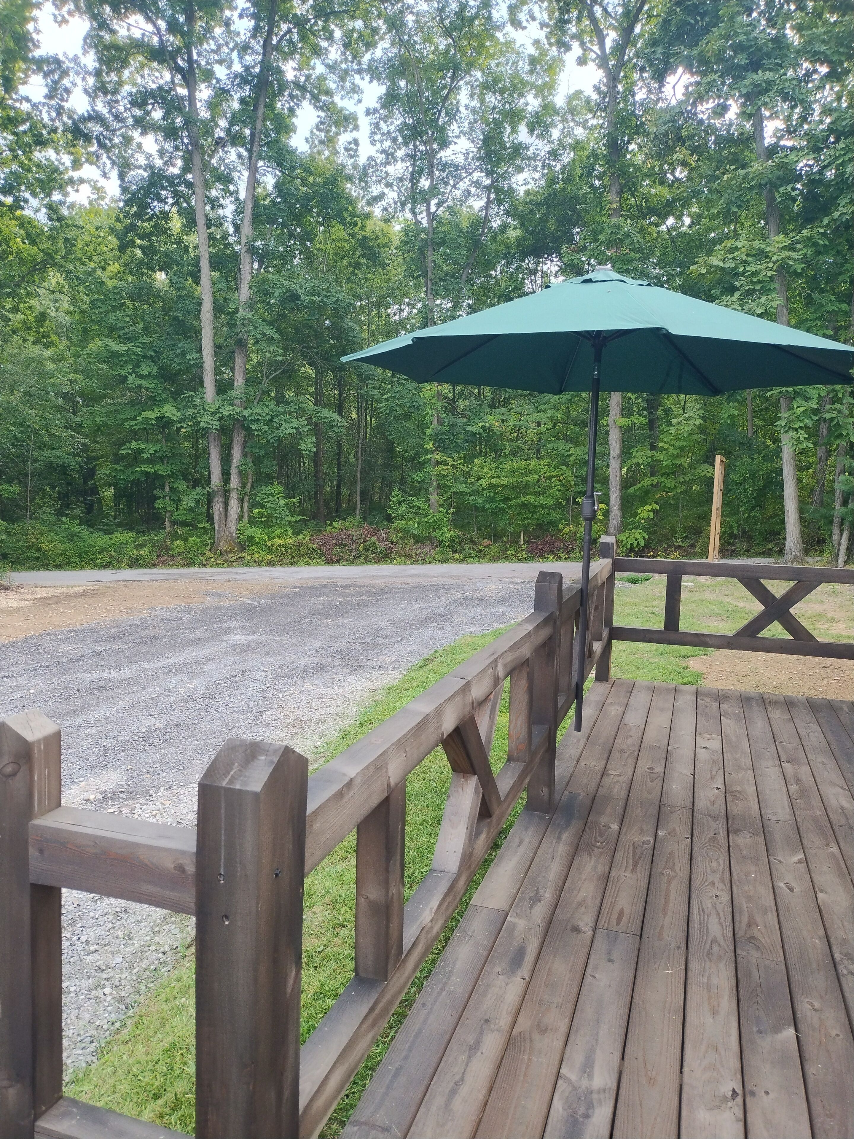 A wooden deck with a green umbrella, surrounded by a wooden fence and trees.