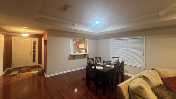 A living room with hardwood flooring, a dining table with chairs, a sofa, a kitchen area with a window, and a door. - Near ACOM and hospital , 2-bedroom house in charming Dothan with WiFi, AC.  (Dothan)