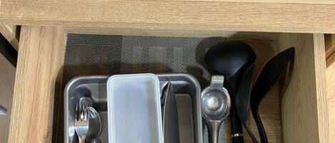 A kitchen drawer with utensils and a plastic container.