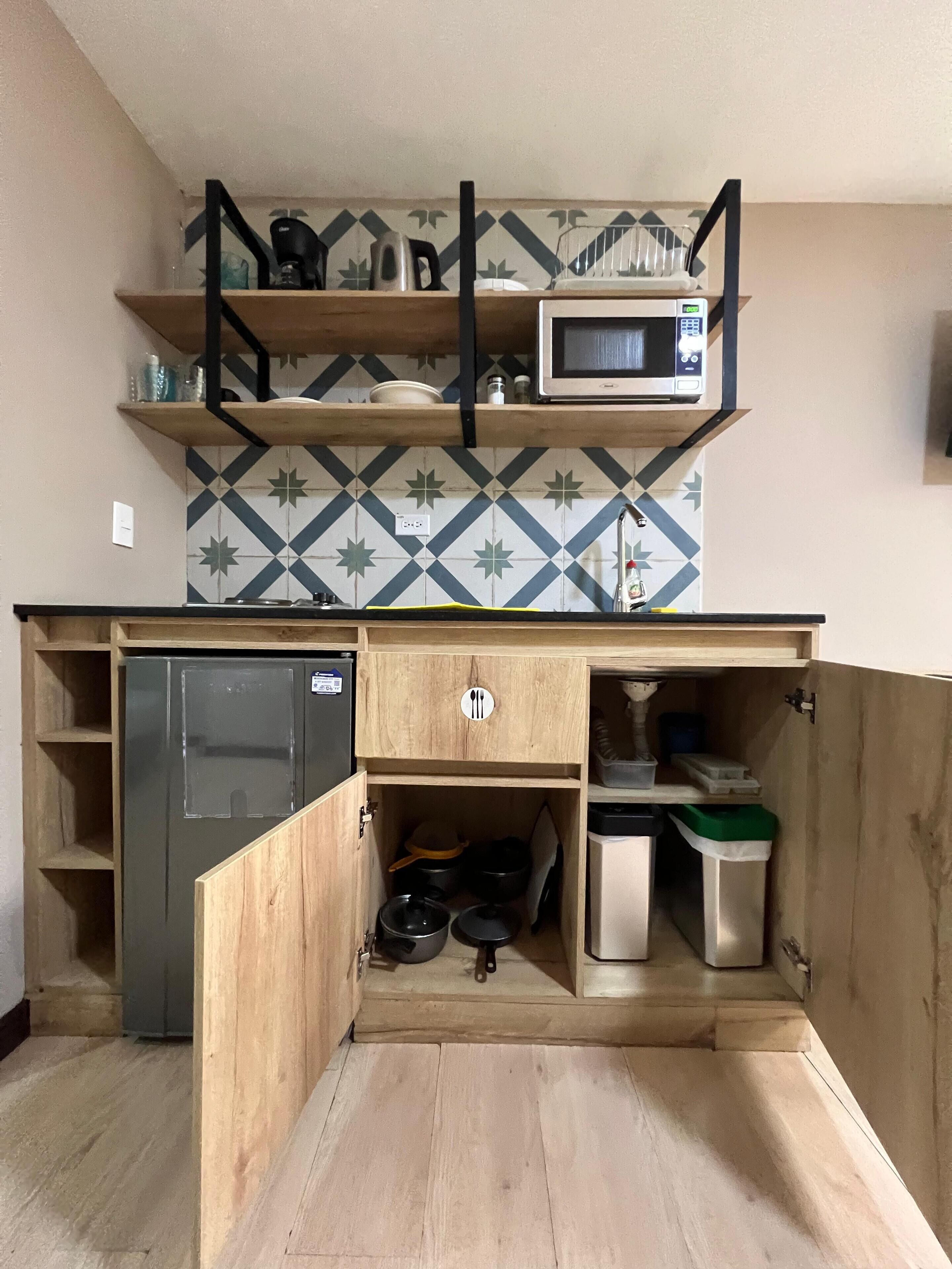 Una cocina compacta con microondas, hervidor y estantes.