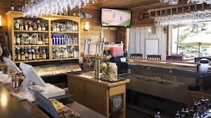 Zona de bar con mostrador, estantes llenos de botellas de licor, un televisor y una ventana con sombrilla.
