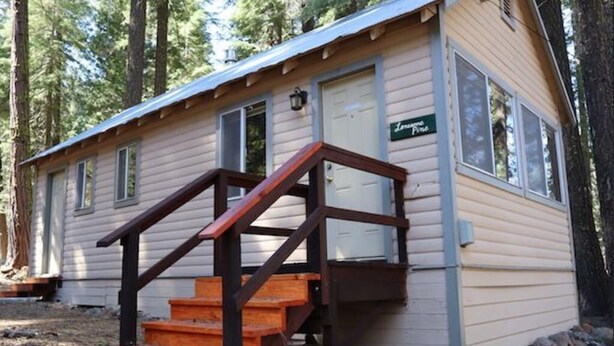 Una cabaña pequeña con una escalera de madera que lleva a una puerta con la inscripción 'Lodge Pine'.