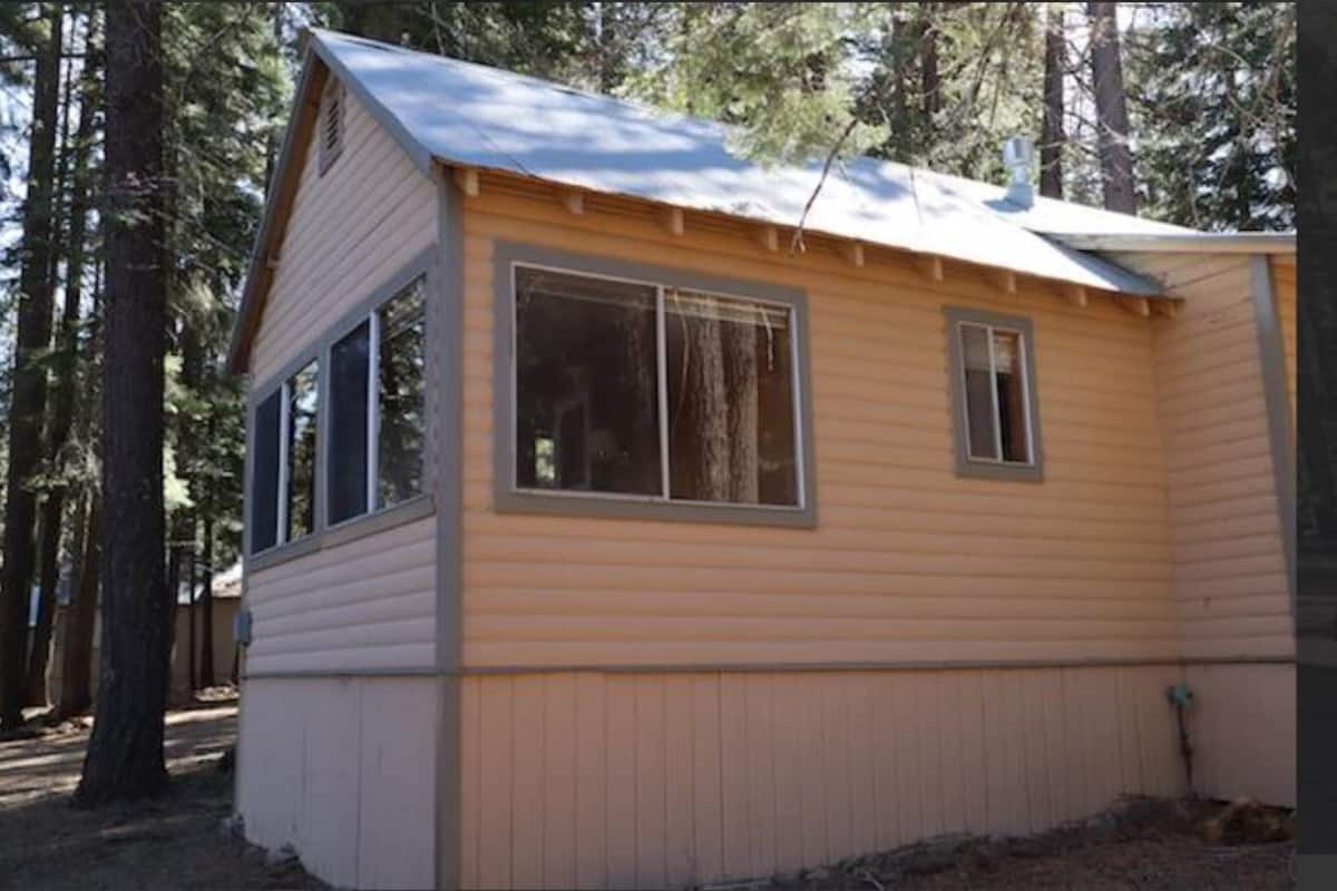Una pequeña cabaña de madera con dos ventanas, techo a dos aguas y chimenea.