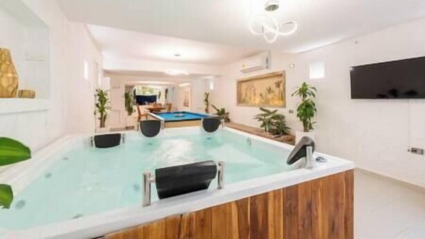 Une piscine intérieure moderne avec une terrasse en bois, une table de billard et un téléviseur fixé au mur.