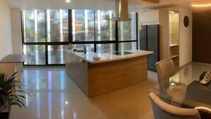 A modern kitchen with a central island, large windows, and a glass dining table. - The Aragon El Poblado Lofts Triplex w/Penthouse (Medellín)