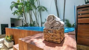 Eine Steinskulptur auf einer Holzplattform, im Hintergrund ein Pool und Palmen.