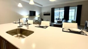 Une cuisine moderne dotée d’un grand îlot central, d’un évier en acier inoxydable et de luminaires suspendus.