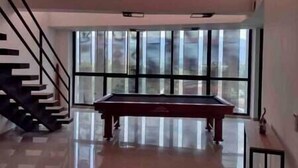 Une pièce spacieuse avec une table de billard, de grandes fenêtres et un escalier.