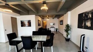 Un espace repas moderne avec une table en verre et des chaises noires, un téléviseur à écran plat et une plante en pot.