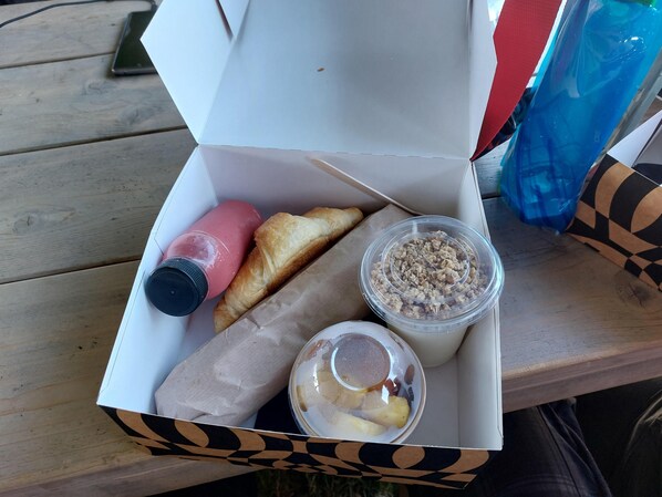 Une boîte contenant une bouteille, un croissant, un récipient de granola et un petit bol avec une cuillère.