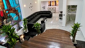 A modern living room with a curved black sofa, a stained glass window, and a wooden staircase leading to a dining area.