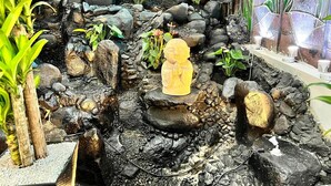 A rock garden with a Buddha statue, surrounded by various plants and a stone wall.
