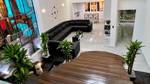 A modern living room with a curved black sofa, a wooden staircase, and a stained glass window.