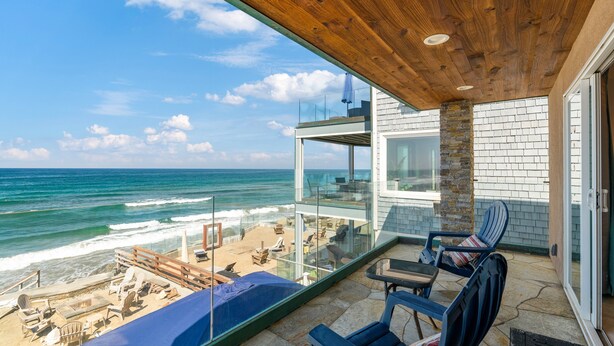 Ein Balkon mit Meerblick, ausgestattet mit Stühlen und einem Tisch, und einer Glasbrüstung.