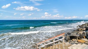 Ein felsiger Strand mit Wellen, einer Holztreppe und blauem Himmel.