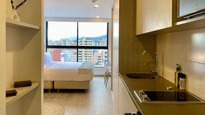 Een moderne hotelkamer met een bed, uitzicht op de stad, een kitchenette en een groot raam.