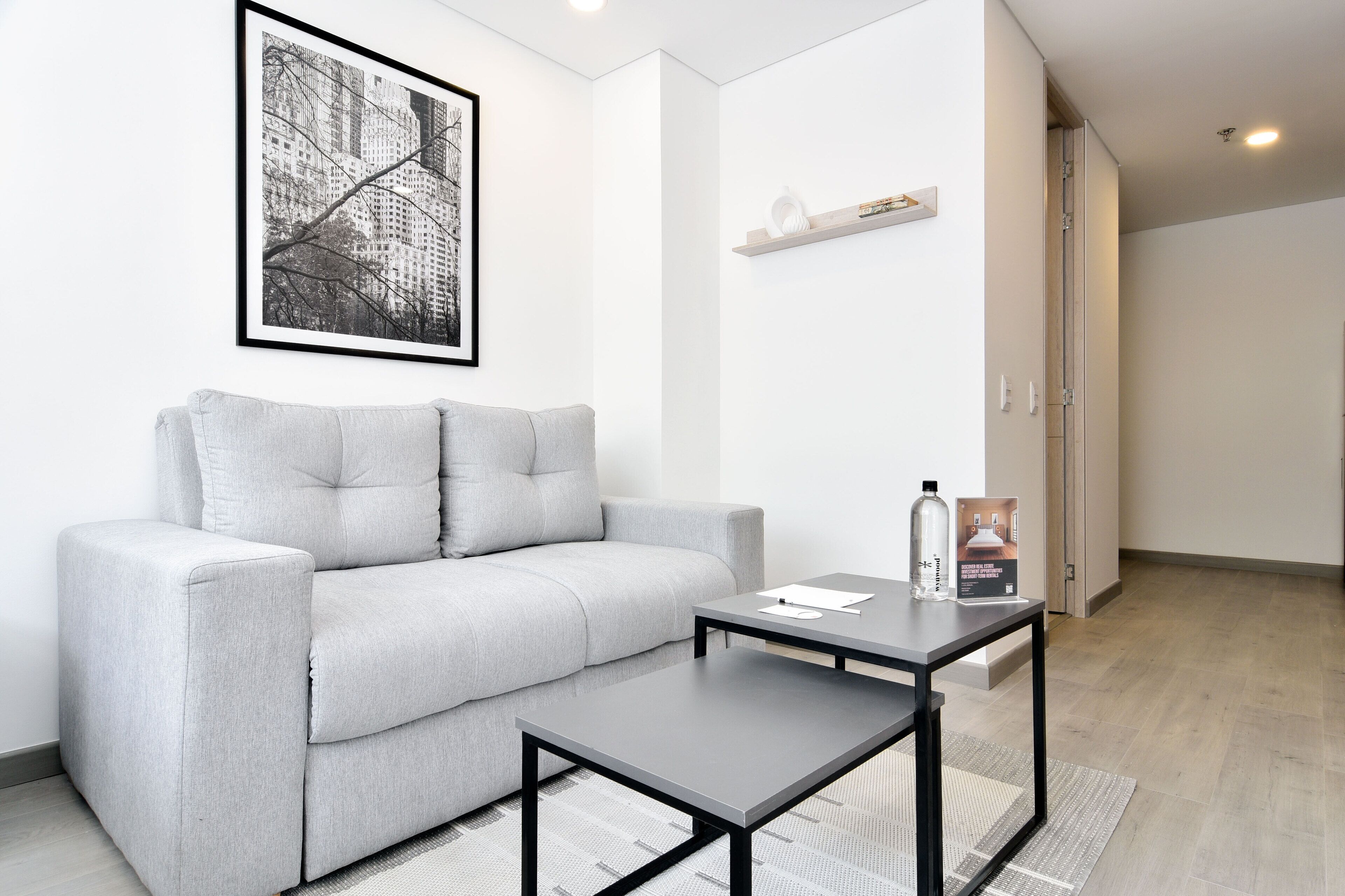 Ein modernes Wohnzimmer mit einem grauen Sofa, einem schwarzen Couchtisch und einem gerahmten Stadtbild an der Wand.
