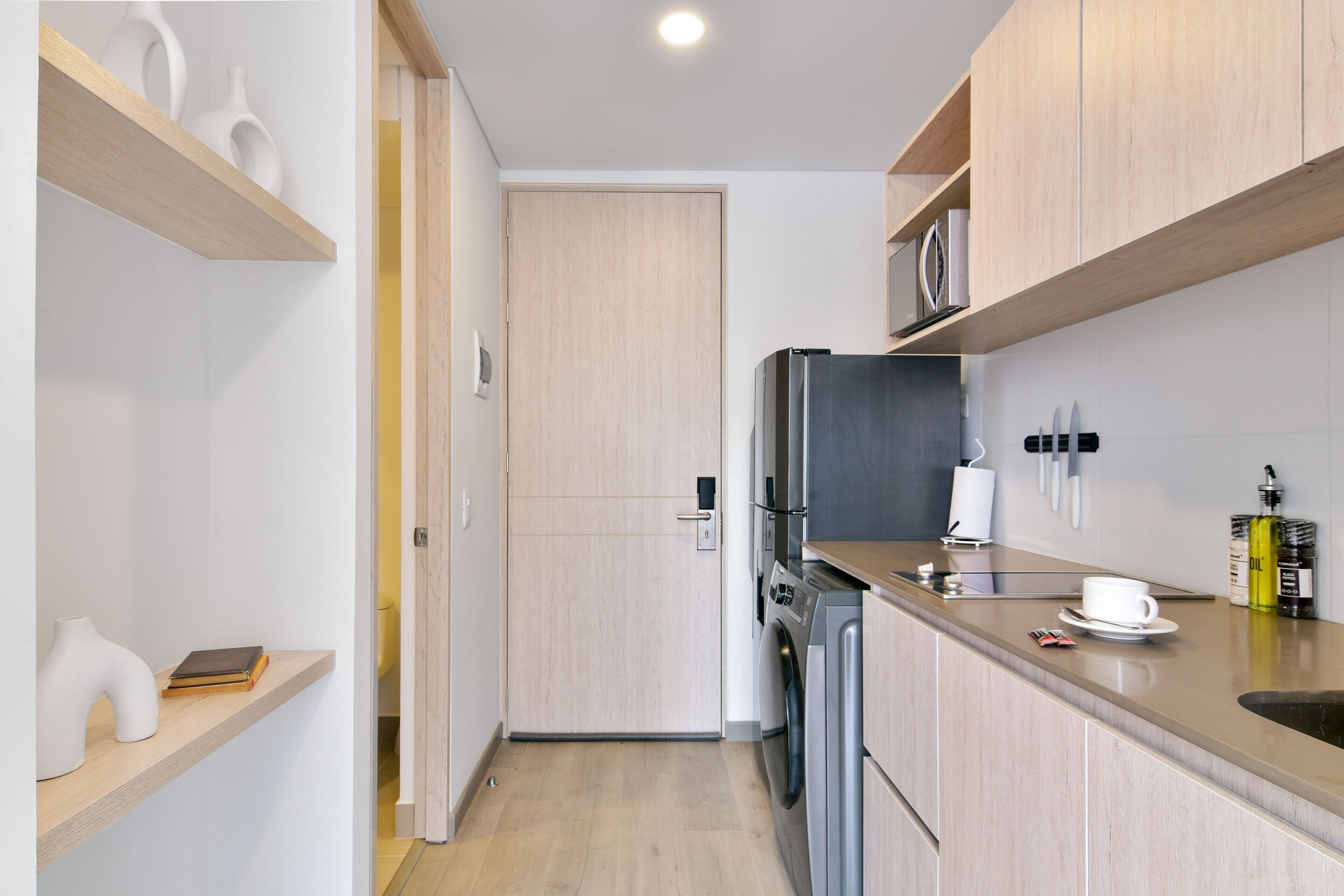 A compact kitchen with wooden cabinets, a built-in washing machine, and a microwave.