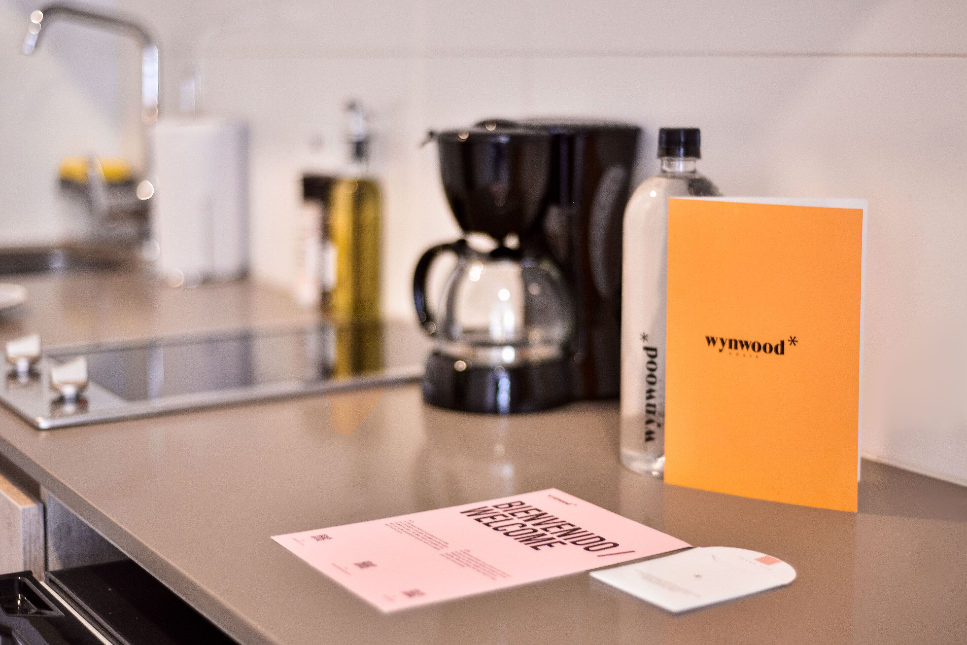 A kitchen counter with a coffee maker, a bottle of water, and a welcome card.