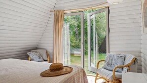 Una habitación acogedora con una cama, un sillón de mimbre y un amplio ventanal corredera que da a un jardín.