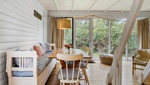 Una habitación acogedora con suelo de madera, un sofá, una mesa de comedor con sillas y un ventanal con vistas al verdor.