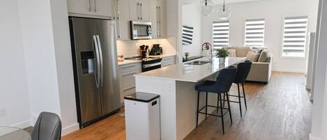 Una cocina moderna con una isla central, electrodomésticos de acero inoxidable y un comedor con mesa de vidrio.