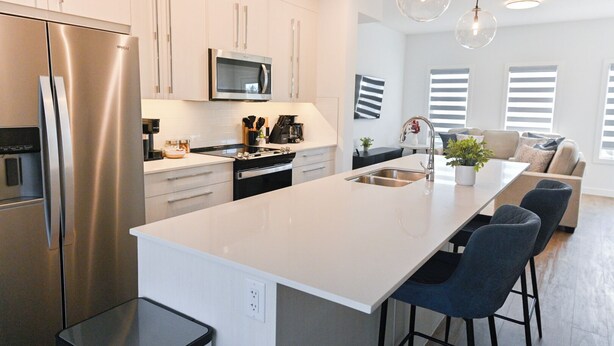 A modern kitchen with a stainless steel refrigerator, a microwave, and a large island with bar stools.