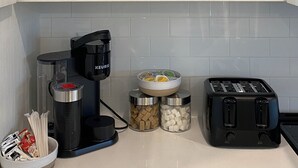 A kitchen with white cabinets, a coffee maker, a toaster, and various mugs and cups on the shelves.