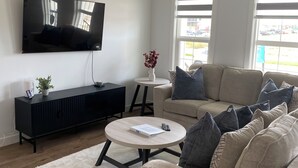 A modern living room with a flat-screen TV, a black entertainment unit, a beige sofa, and a round coffee table.