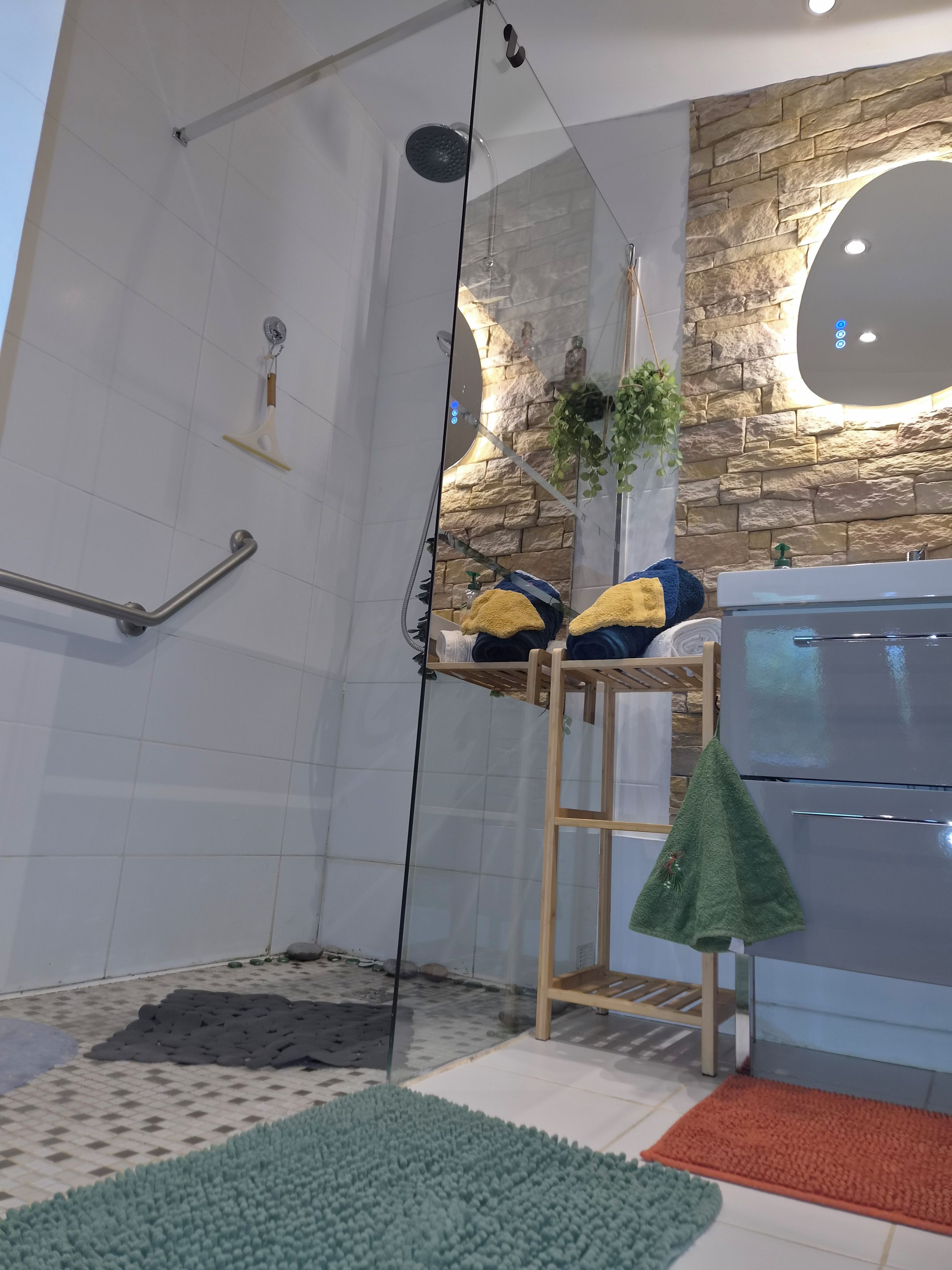 A modern bathroom with a glass shower enclosure, a stone accent wall, and a built-in sink with a towel rack.
