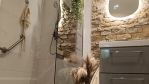 Un baño moderno con cabina de ducha de vidrio, pared de piedra, espejo redondo y tocador de madera.