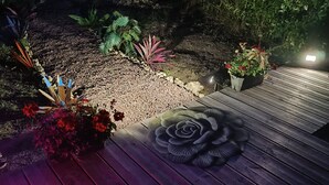 A wooden deck with a decorative flower pattern, surrounded by various plants and a wooden fence. - Vila Sozinha Luxury (Escames)
