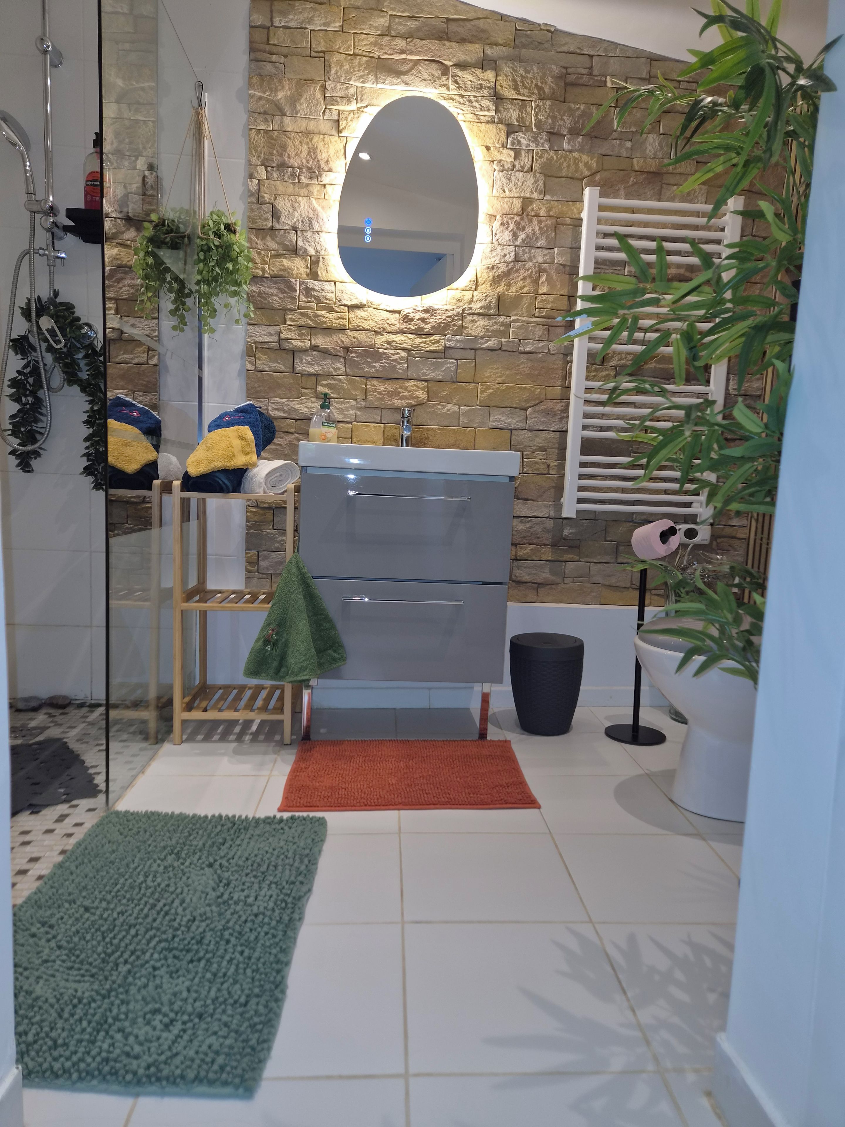 A bathroom with a stone wall, a mirror, a sink, a towel rack, and a shower.