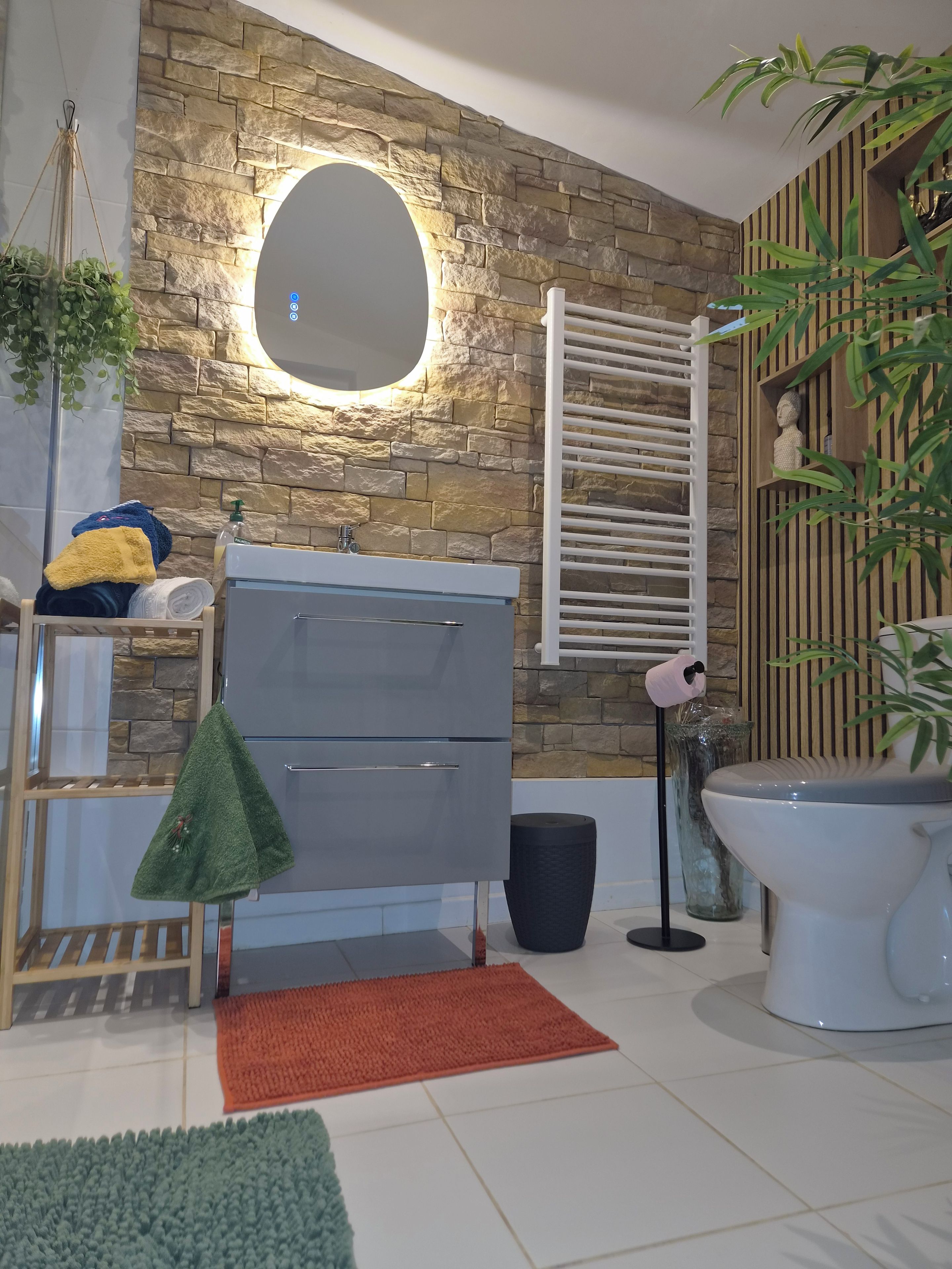 Un baño con pared de piedra, un espejo redondo, un inodoro blanco, un lavabo y un estante con adornos.
