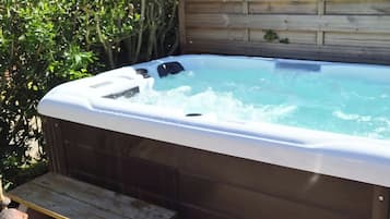 A hot tub with a wooden bench in front, surrounded by greenery.