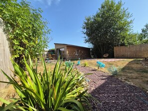 Ein Garten mit einem Holzhaus, einem umzäunten Bereich und verschiedenen Pflanzen.