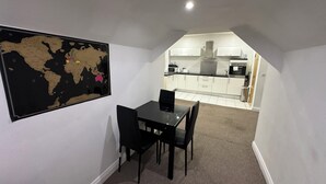 A dining area with a black table and chairs, a world map on the wall, and a view into a modern kitchen with white cabinets and appliances.
