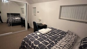 A bedroom with a bed, a desk, a chair, a mirror, and a window with blinds.