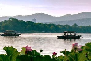 A calm lake with boats and lotus flowers in the foreground. - Wuyang International Hotel (Hangzhou)