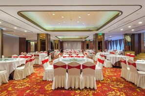 Un salón de banquetes con mesas redondas, sillas blancas y cintas rojas.