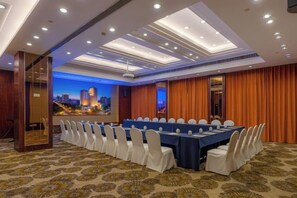 Un salón de conferencias con una larga mesa, sillas blancas y vistas a la ciudad.